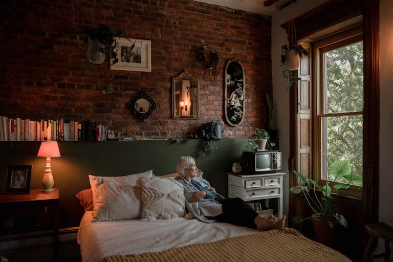 A senior woman relaxing in a cozy bedroom with vintage decor and natural light.